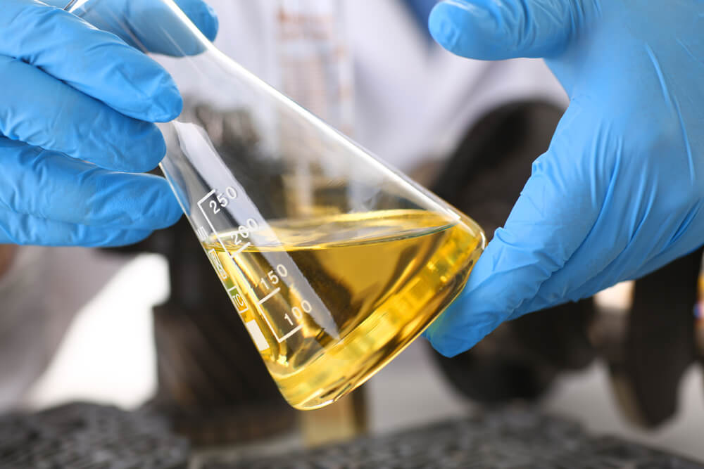 Close up of gloved hands holding a chemistry test tube filled with lubricant
