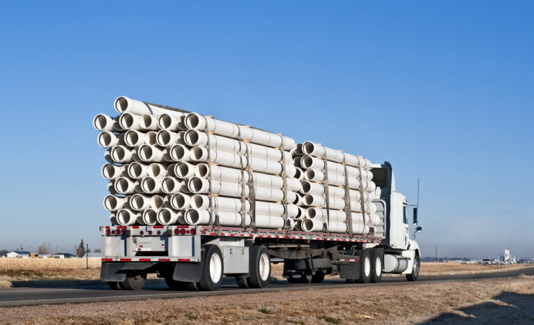 Flatbed truck carrying large pipes.