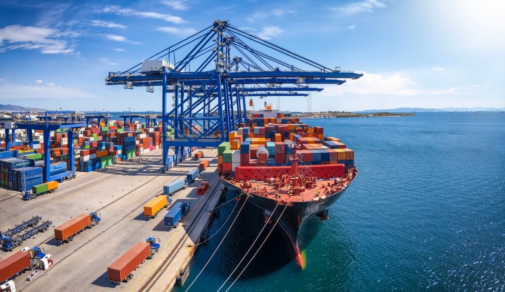 Docked cargo ship with shipping containers loaded onto it. With cranes and equipment in the background.