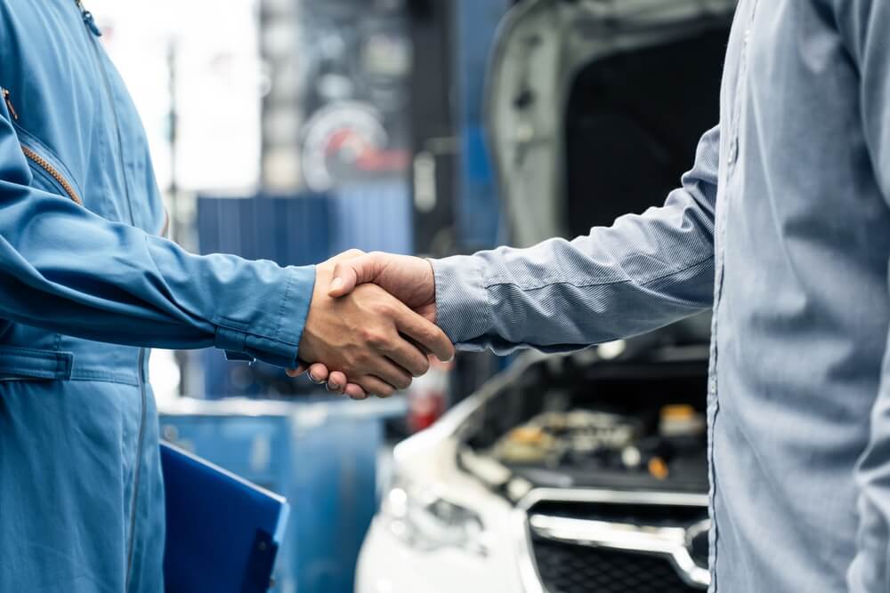 Vehicle mechanic shaking hands with a sales man. Car with open bonnet in the background.
