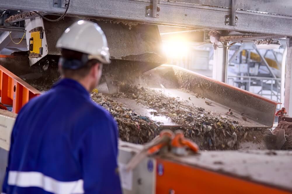 Worker at a waste and recycling centre overseeing waste being sorted on a conveyor belt.