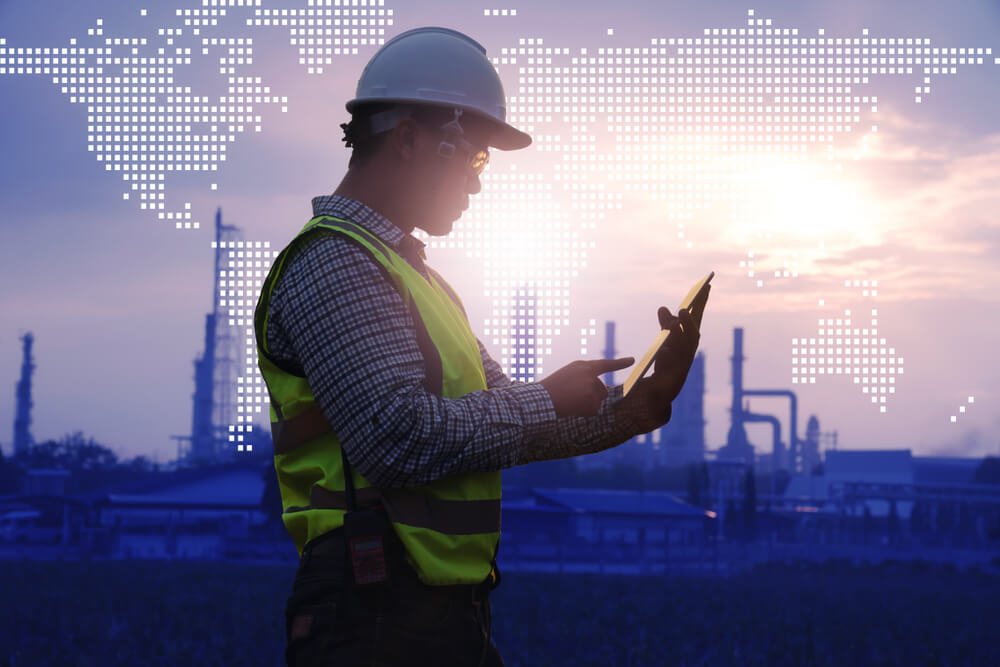 Concept image. Engineer holding tablet computer with industrial plant and world map in the background.
