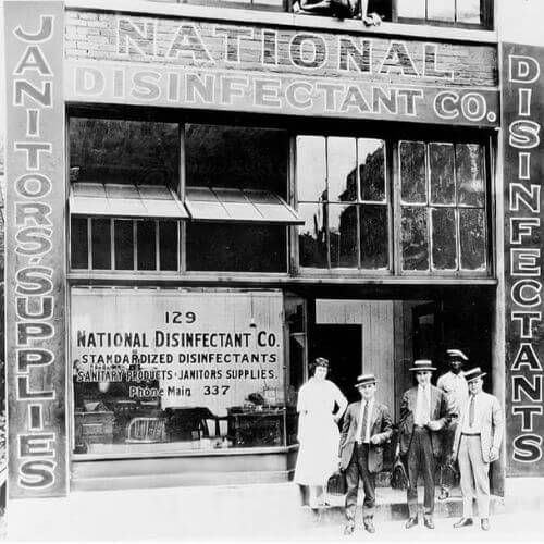 Black and white photograph of the first National Disinfectant building with people stood in the doorway posing for the photo.