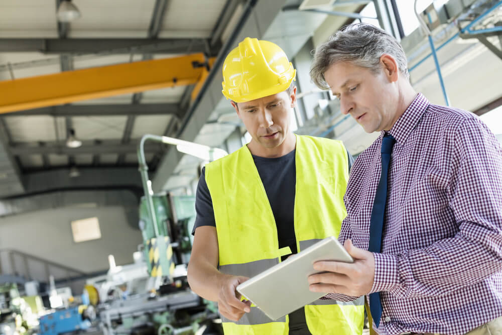 Supervisor and manual worker using digital tablet in metal industry